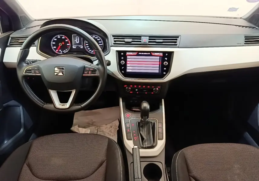 Vue intérieure frontale du tableau de bord et volant noir de la SEAT Arona 2019 avec écran tactile central allumé.