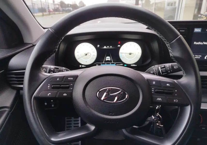 Vue intérieure centrée sur le volant noir de la Hyundai Bayon 2022 avec tableau de bord numérique et commandes intégrées.
