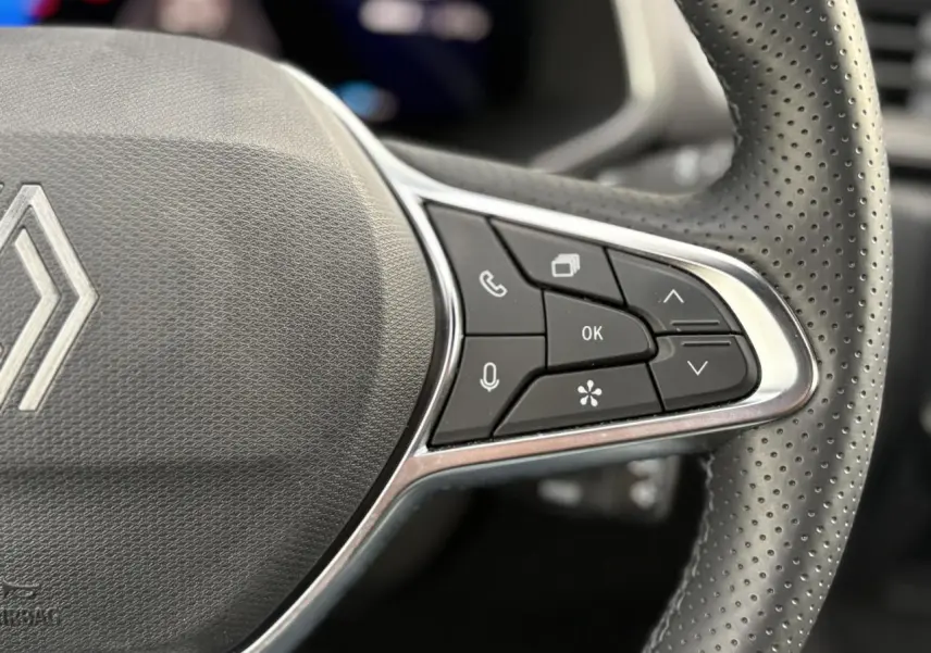 Gros plan sur le volant en cuir perforé du Renault Symbioz bleu, avec commandes multifonctions et logo central.