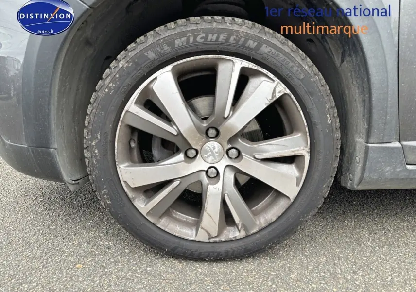Gros plan sur la roue avant gauche d'un Peugeot 2008 gris platinium avec jante alliage et logo lion central.