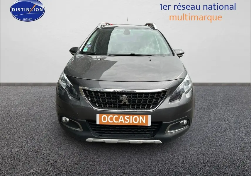 Vue frontale d'un Peugeot 2008 gris platinium de 2019 avec calandre noire et phares allumés sur fond neutre.