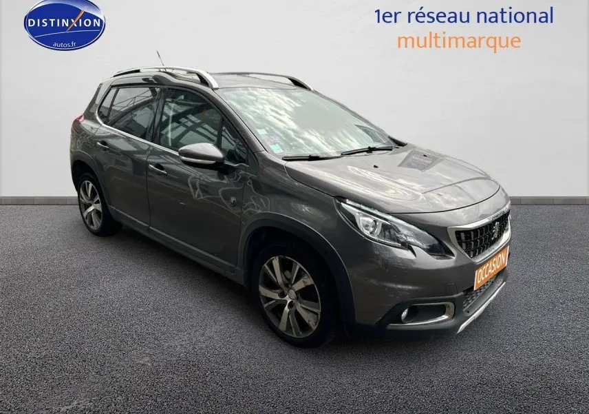 Peugeot 2008 gris platinium en 3/4 avant droit, avec jantes alliage et barres de toit visibles.