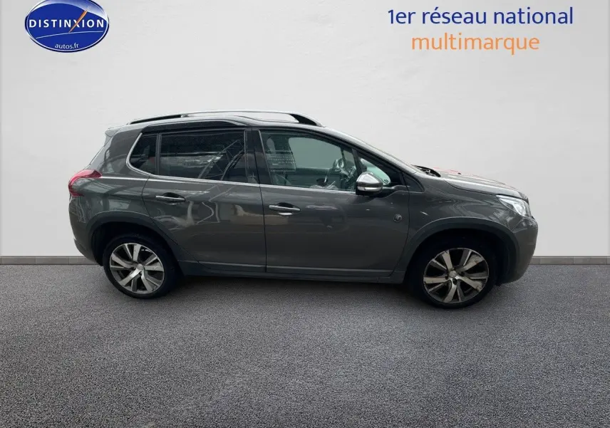 Profil côté gauche d'un Peugeot 2008 gris platinium de 2019 avec jantes alliage et barres de toit visibles.