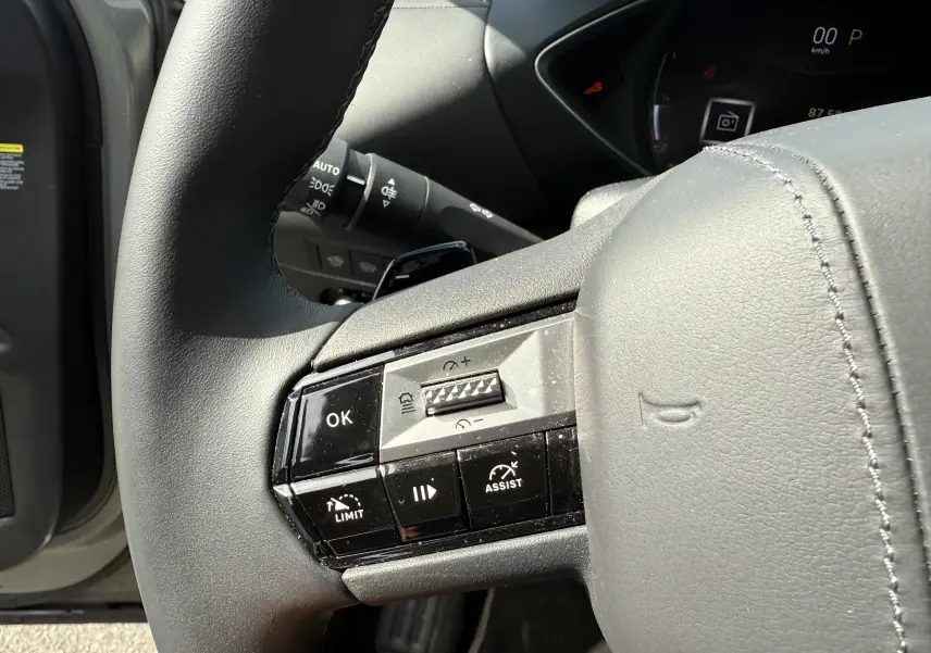 Gros plan sur le volant gris du DS3 2024 avec commandes multifonctions et tableau de bord partiellement visible.