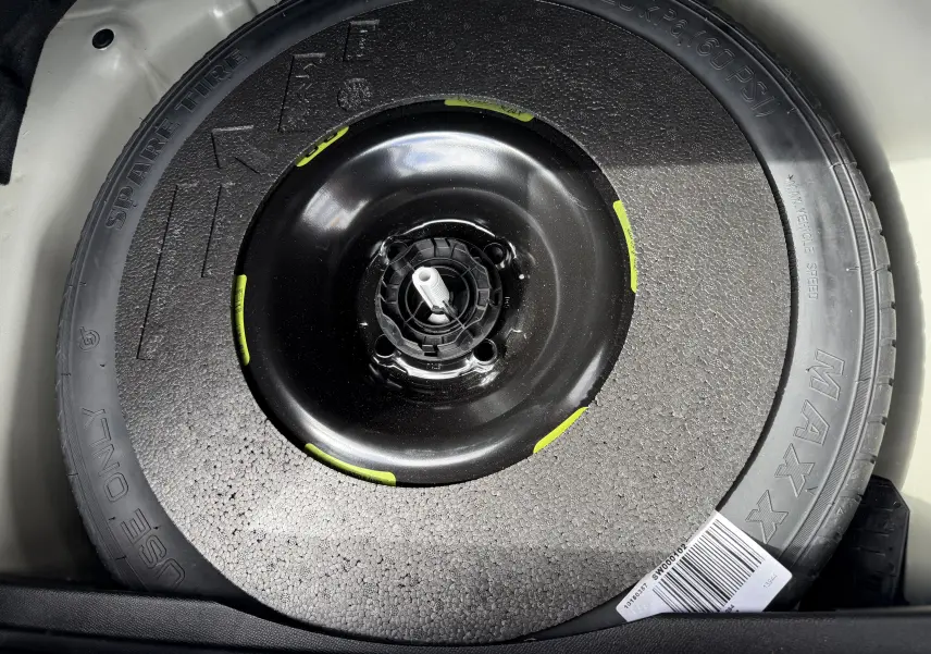Gros plan sur la roue de secours noire du coffre d'une DS3 2024 gris laqué toit noir, version BlueHDi 130 EAT8 Opera.