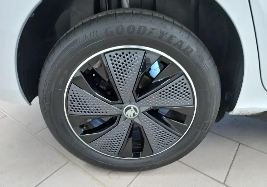 Gros plan sur la roue avant gauche d'un Skoda Kamiq blanc Lune avec jante noire au design perforé.
