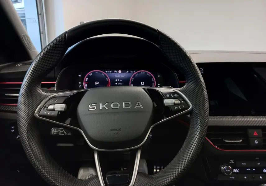 Vue centrée sur le volant perforé SKODA du KAMIQ 2025 avec tableau de bord numérique et détails intérieurs noirs et rouges.