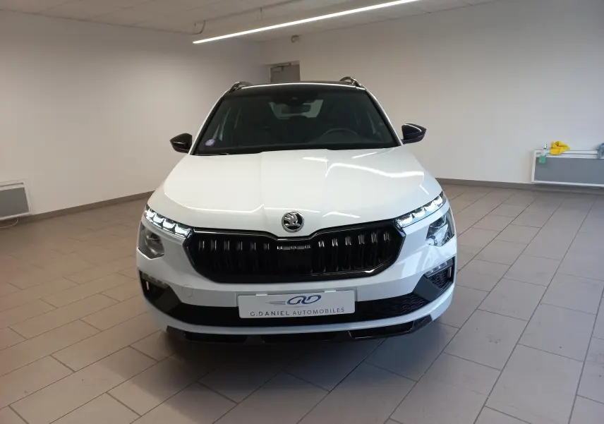 Vue frontale d'un Skoda Kamiq 2025 blanc Lune avec calandre noire et feux LED allumés en intérieur showroom.