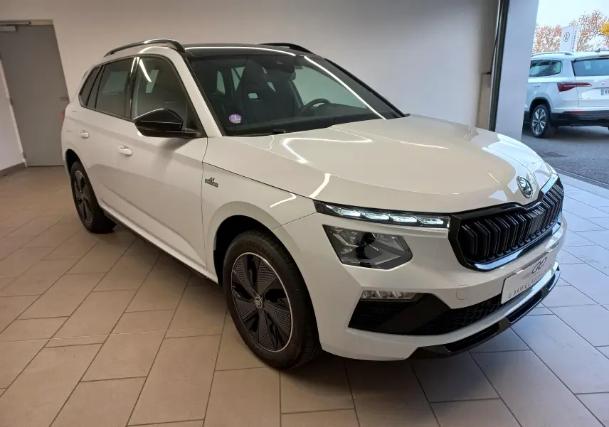 Vue 3/4 avant d'un Skoda Kamiq blanc Lune 2025 avec calandre noire et jantes noires distinctives Monte-Carlo.