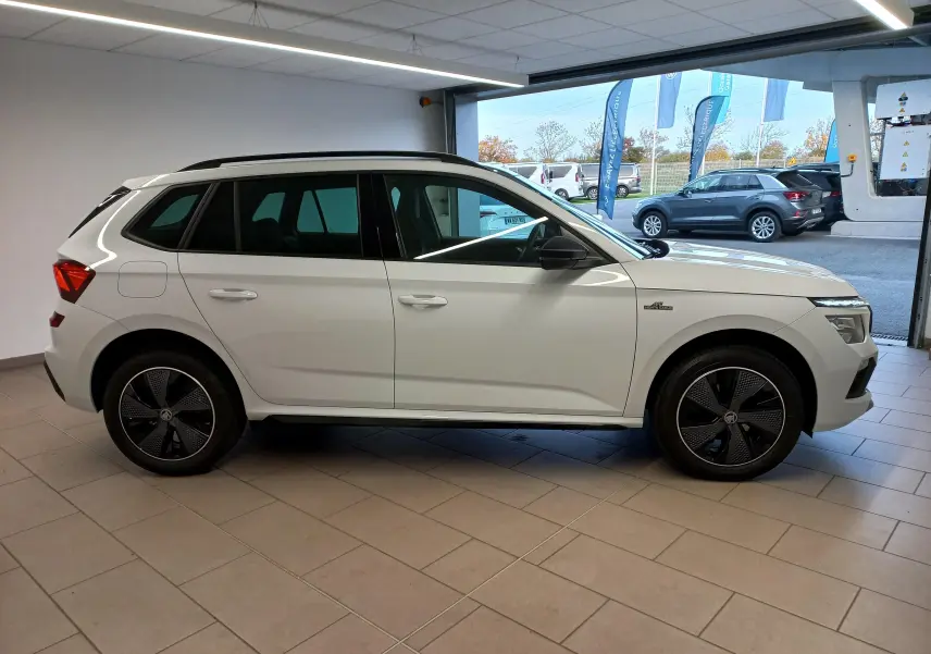 Vue de profil côté gauche d'un Skoda Kamiq 2025 blanc Lune avec jantes noires et badge Monte-Carlo visible sur l'aile avant.