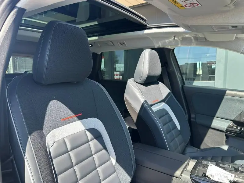 Vue intérieure côté avant droit du Citroën C5 Aircross 2026, sièges tissu et cuir noir avec surpiqûres blanches et toit ouvrant panoramique.