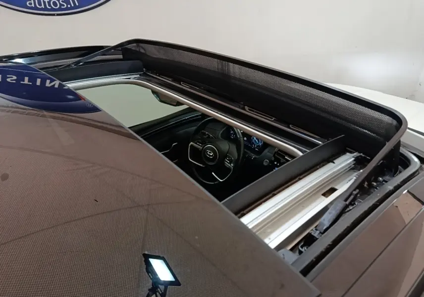 Vue plongeante sur le toit ouvrant électrique ouvert d’un Hyundai Tucson blanc, avec aperçu du tableau de bord intérieur.