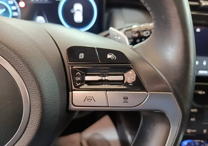 Gros plan sur les commandes du volant noir du Hyundai Tucson 1.6 Hybrid 230 Executive, avec boutons multifonctions visibles.