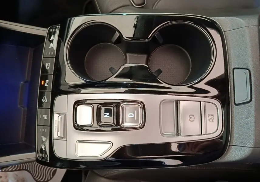 Vue plongeante sur la console centrale noire brillante du Hyundai Tucson 1.6 Hybrid 230 Executive avec commandes de boîte auto et porte-gobelets.