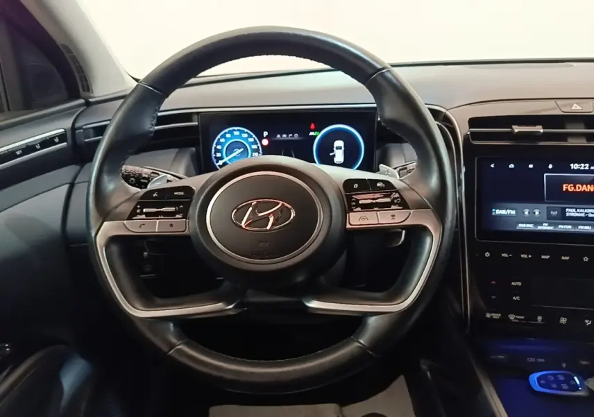 Vue intérieure centrée sur le volant noir du Hyundai Tucson 1.6 Hybrid 230 Executive avec tableau de bord digital.