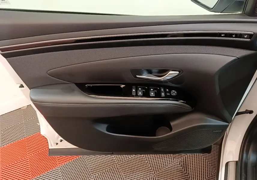 Vue intérieure de la porte avant gauche blanche d'un Hyundai Tucson 1.6 Hybrid 230 Executive avec commandes et habillage noir.