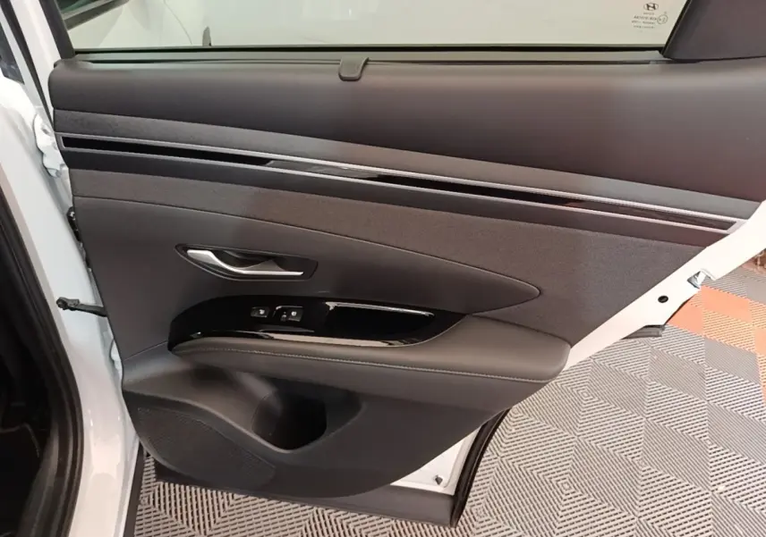 Vue intérieure de la porte arrière gauche blanche du Hyundai Tucson 1.6 Hybrid 230 Executive avec garniture noire et commandes de fenêtre.