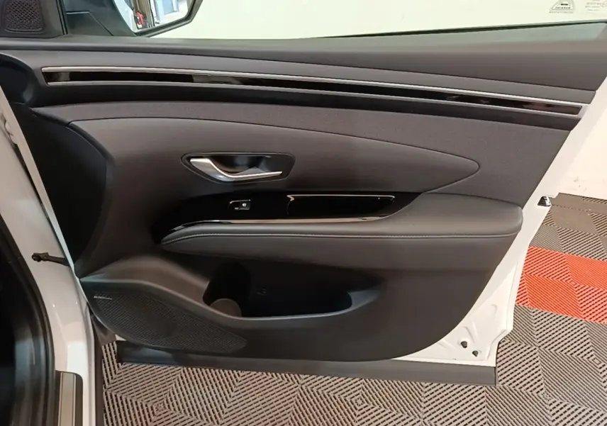 Vue intérieure de la porte avant gauche du Hyundai Tucson blanc, avec garniture noire et poignée argentée.