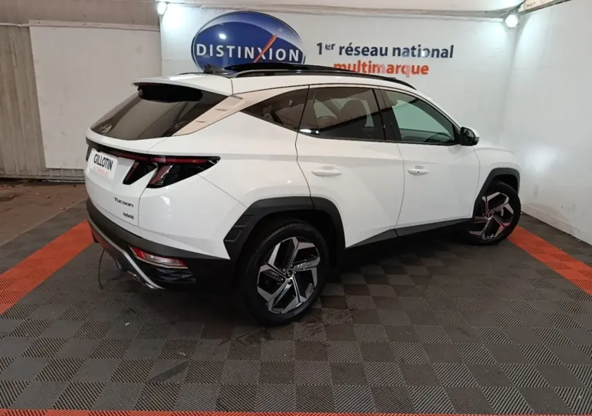 Vue 3/4 arrière droite d’un Hyundai Tucson blanc 2022 avec jantes noires et toit noir dans un showroom.