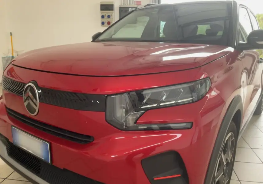 Vue 3/4 avant droite d'une Citroën C3 ë-113 Berline Max rouge métal foncé avec calandre noire et phares modernes.