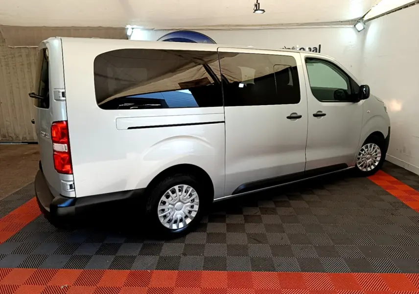 Vue 3/4 arrière droite du Toyota Proace Verso gris clair avec vitres teintées et jantes acier en intérieur showroom.