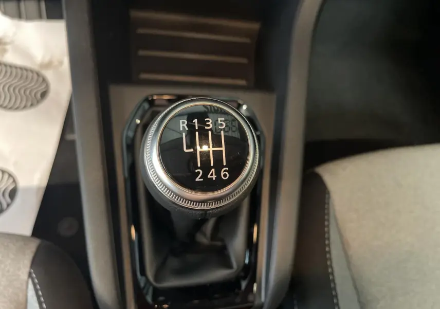 Gros plan sur le levier de vitesses manuel de la Renault Clio blanche, entouré de la console noire et sièges gris.