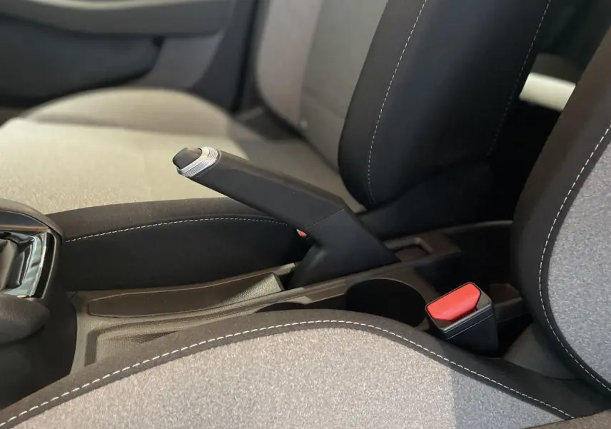 Gros plan sur frein à main manuel et ceinture rouge entre sièges tissu gris et noir de Renault Clio 1.5 Blue dCi 2025.