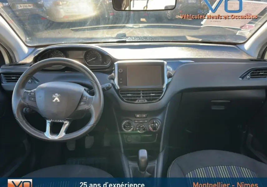 Vue intérieure avant du tableau de bord noir de la Peugeot 208 blanche de 2015 avec écran tactile et volant multifonction.