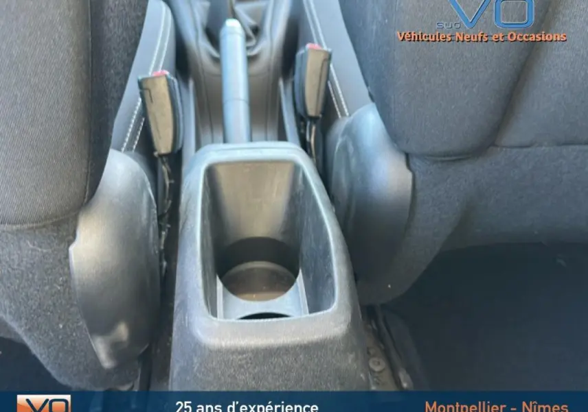 Gros plan sur la console centrale et le frein à main entre les sièges avant noirs d'une Peugeot 208 blanche de 2015.