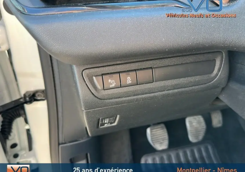 Détail des commandes sous le tableau de bord côté gauche d'une Peugeot 208 blanche de 2015 avec pédales et portière ouverte.