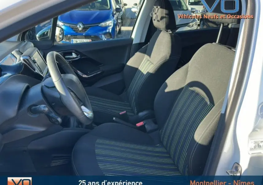 Vue intérieure côté conducteur de la Peugeot 208 blanche de 2015, sièges noirs à rayures vertes et volant visible.