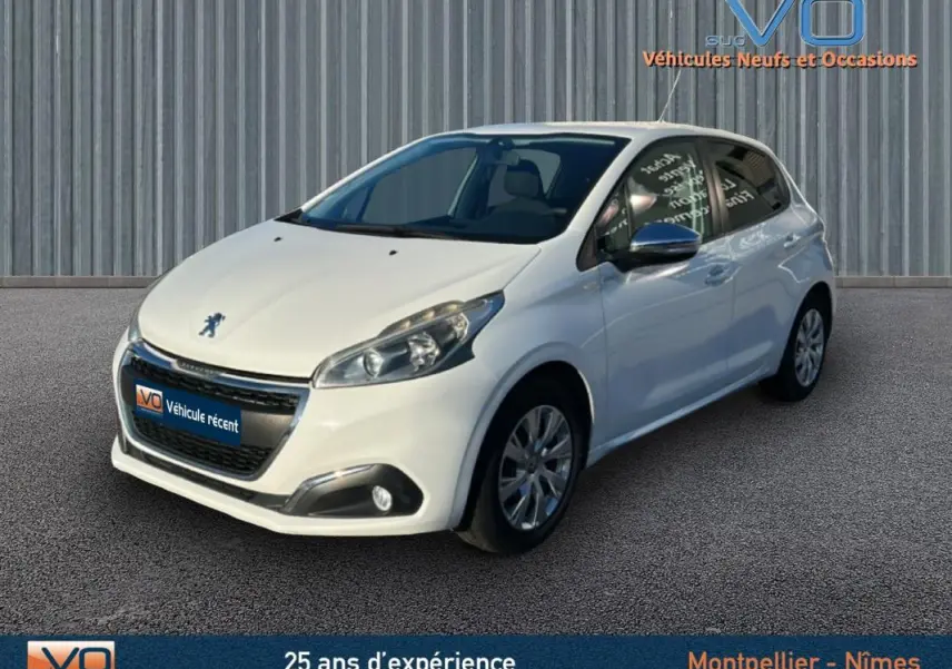 Peugeot 208 blanc vue 3/4 avant droit, avec jantes classiques 15 pouces et phares antibrouillard visibles.