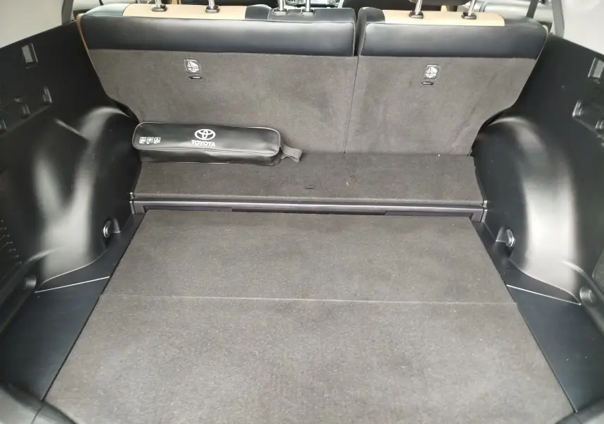 Coffre ouvert du Toyota RAV4 noir cobalt, vue intérieure arrière montrant la moquette et un kit de secours Toyota.