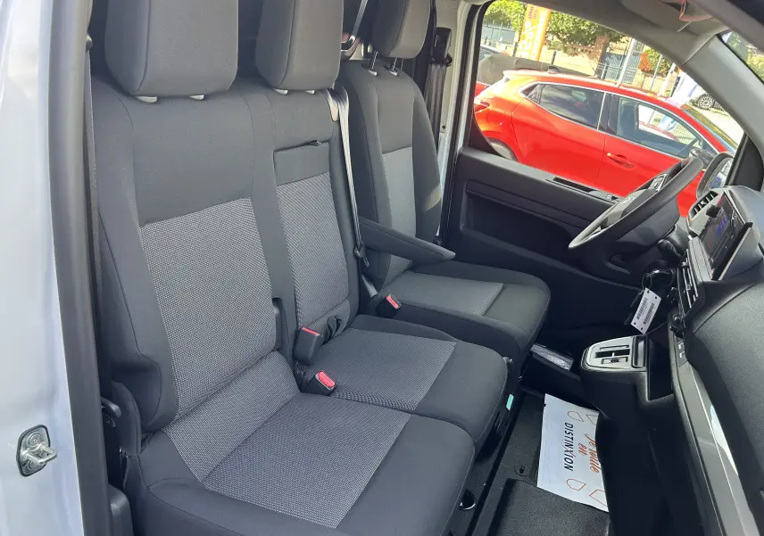 Vue intérieure côté conducteur du Citroën Jumpy blanc 2025, montrant les sièges avant en tissu gris et noir.