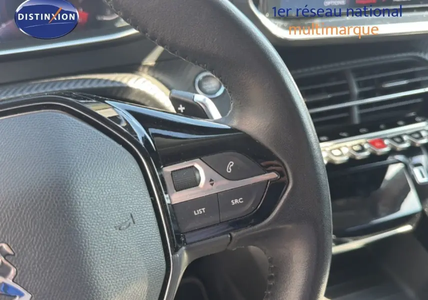 Gros plan sur le volant cuir noir du Peugeot 2008 2020, avec commandes intégrées et tableau de bord en arrière-plan.