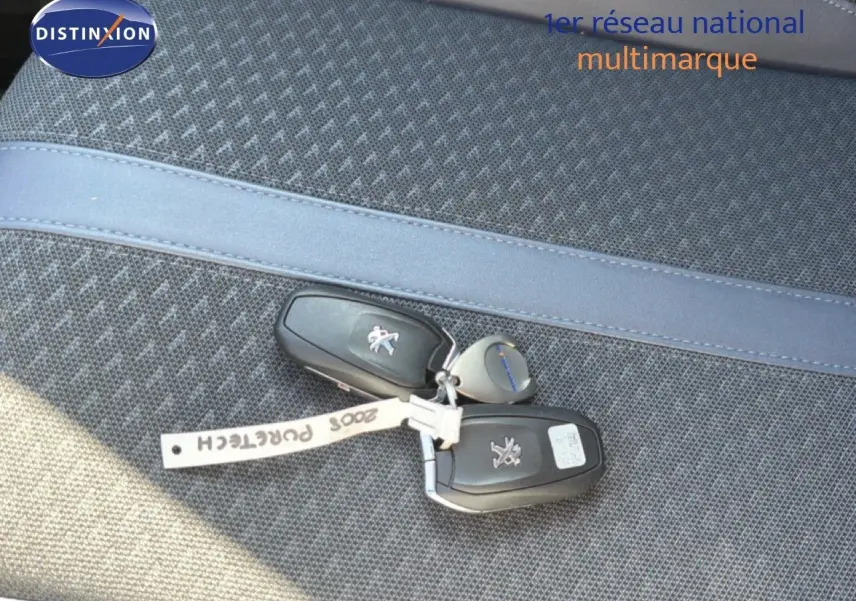 Gros plan sur les clés noires de la Peugeot 2008 posées sur un siège en tissu gris à motif.
