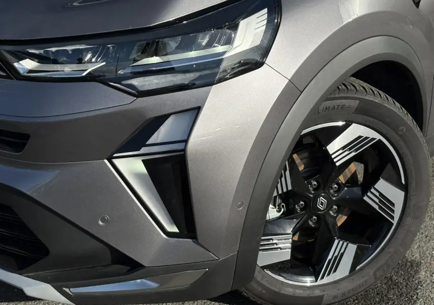 Gros plan sur l'avant droit gris Cassiopée du Renault Symbioz E-Tech, mettant en valeur le phare LED et la jante 18 pouces.
