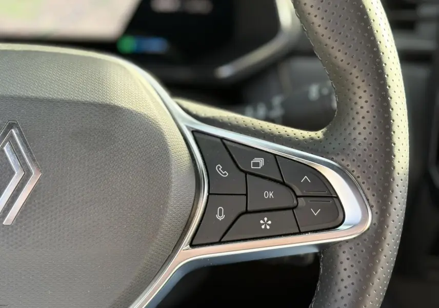 Gros plan sur le côté droit du volant en cuir perforé noir du Renault Symbioz avec commandes intégrées et logo Renault visible.