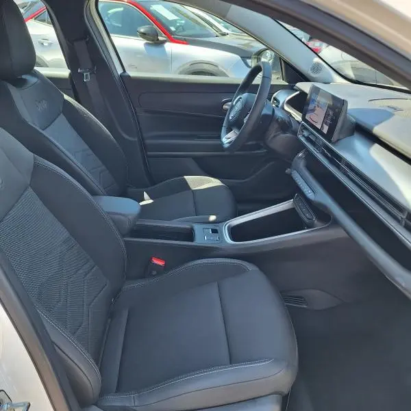 Vue intérieure côté conducteur du Jeep Avenger électrique blanc 2025, sièges noirs avec accoudoir central et écran tactile.