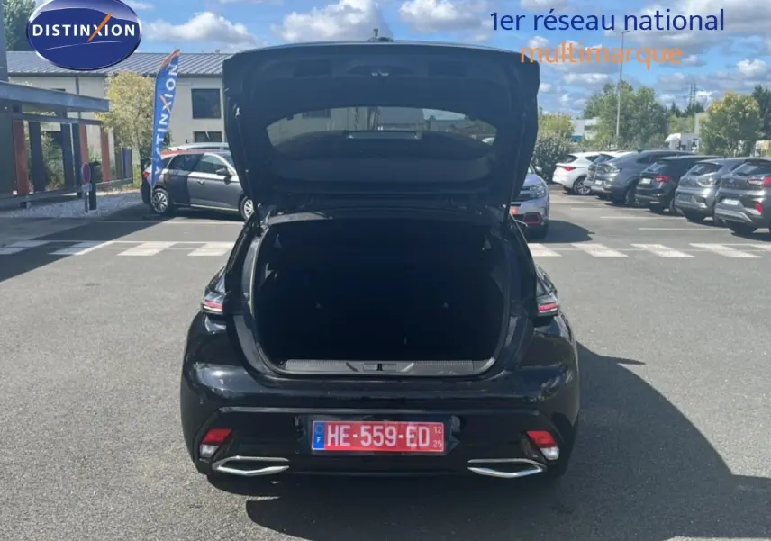Vue arrière d'une Peugeot 308 noir métal 2025 avec coffre ouvert sur un parking ensoleillé.