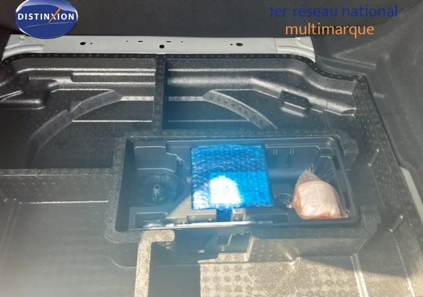 Coffre ouvert de Peugeot 308 noir métal, vue plongeante sur rangement sous plancher avec accessoires emballés.