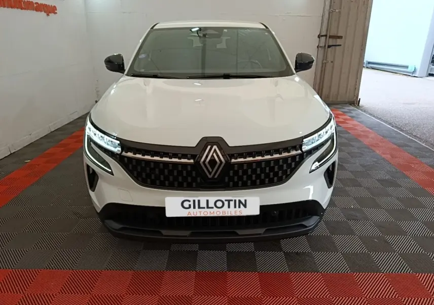 Vue de face du Renault Austral blanc avec calandre noire et phares LED allumés en intérieur showroom.