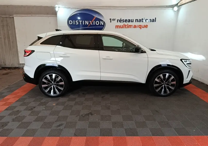 Renault Austral blanc en profil droit dans un showroom, avec jantes alliage et toit spoiler visible.
