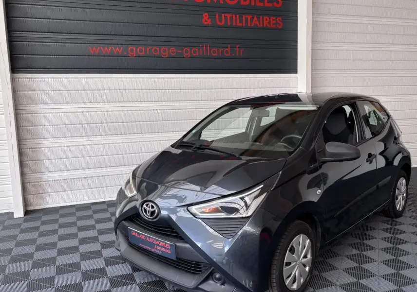 Toyota Aygo 1.0 VVT-i x-black gris foncé vue 3/4 avant droit dans un garage avec sol à damier.