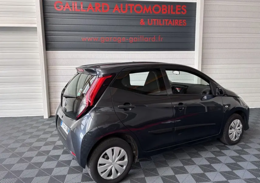 Toyota Aygo 1.0 VVT-i x-black gris foncé vue 3/4 arrière droit dans un garage avec sol damier.