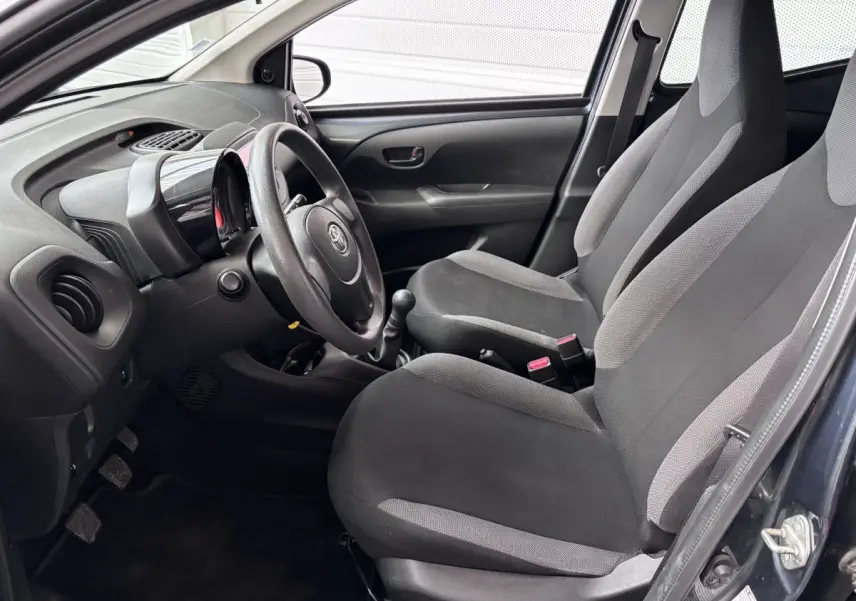 Vue intérieure côté conducteur de la Toyota Aygo 2020, sièges gris et tableau de bord avec volant et levier de vitesse.