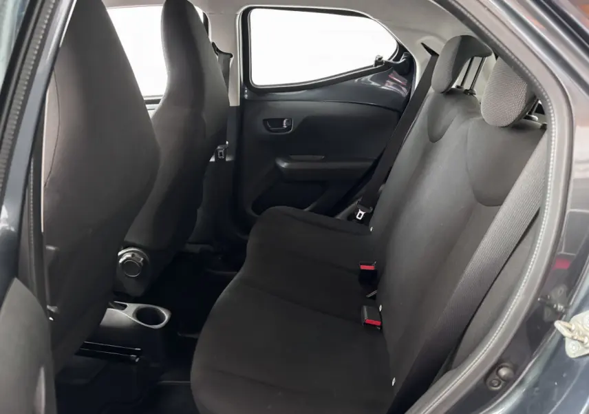 Vue intérieure sur la banquette arrière noire d'une Toyota Aygo gris foncé, avec ceintures et appuie-têtes visibles.