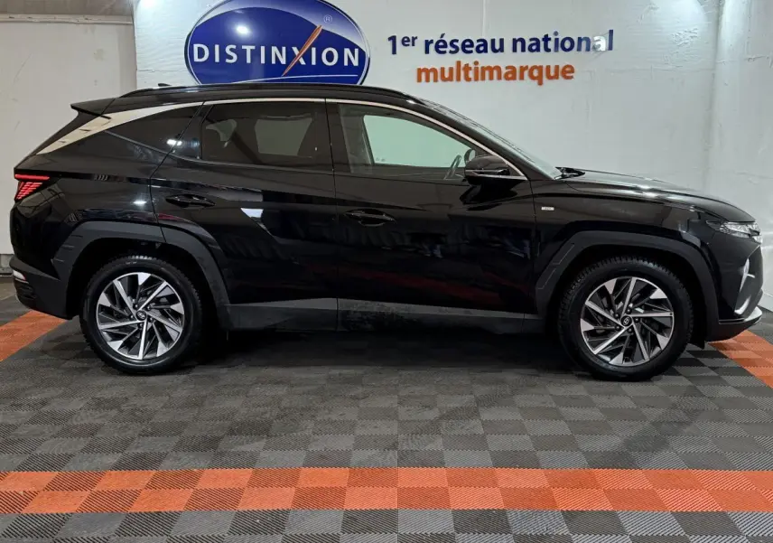 Profil côté gauche du Hyundai Tucson noir 2021 avec jantes alliage et lignes anguleuses modernes, en intérieur showroom.