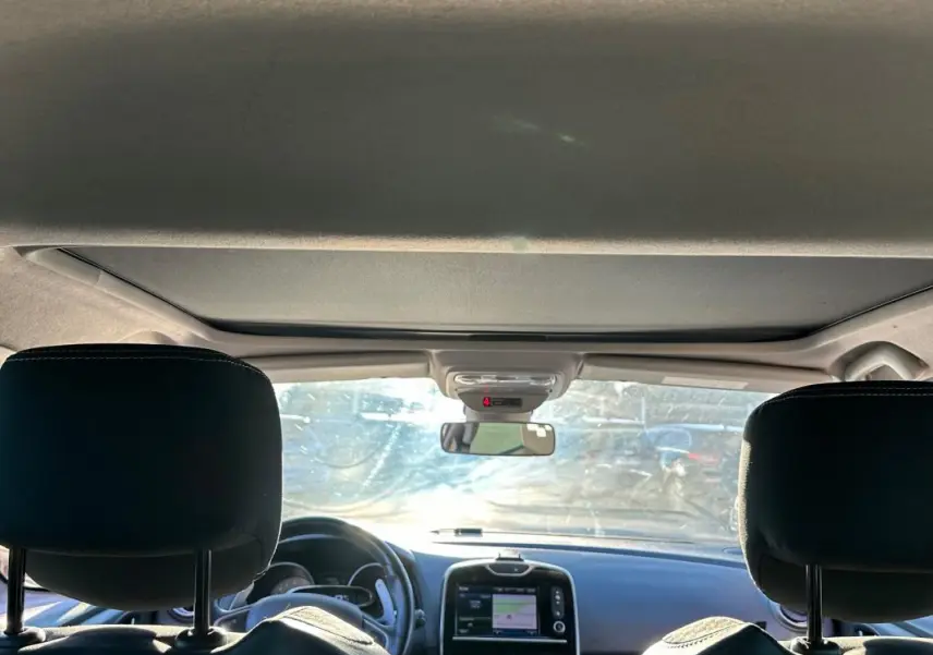 Vue intérieure avant de la Renault Clio IV blanche, montrant tableau de bord avec écran tactile et volant cuir.