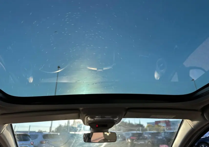 Vue intérieure avant de la Renault Clio IV blanche avec toit panoramique et rétroviseur central visible.